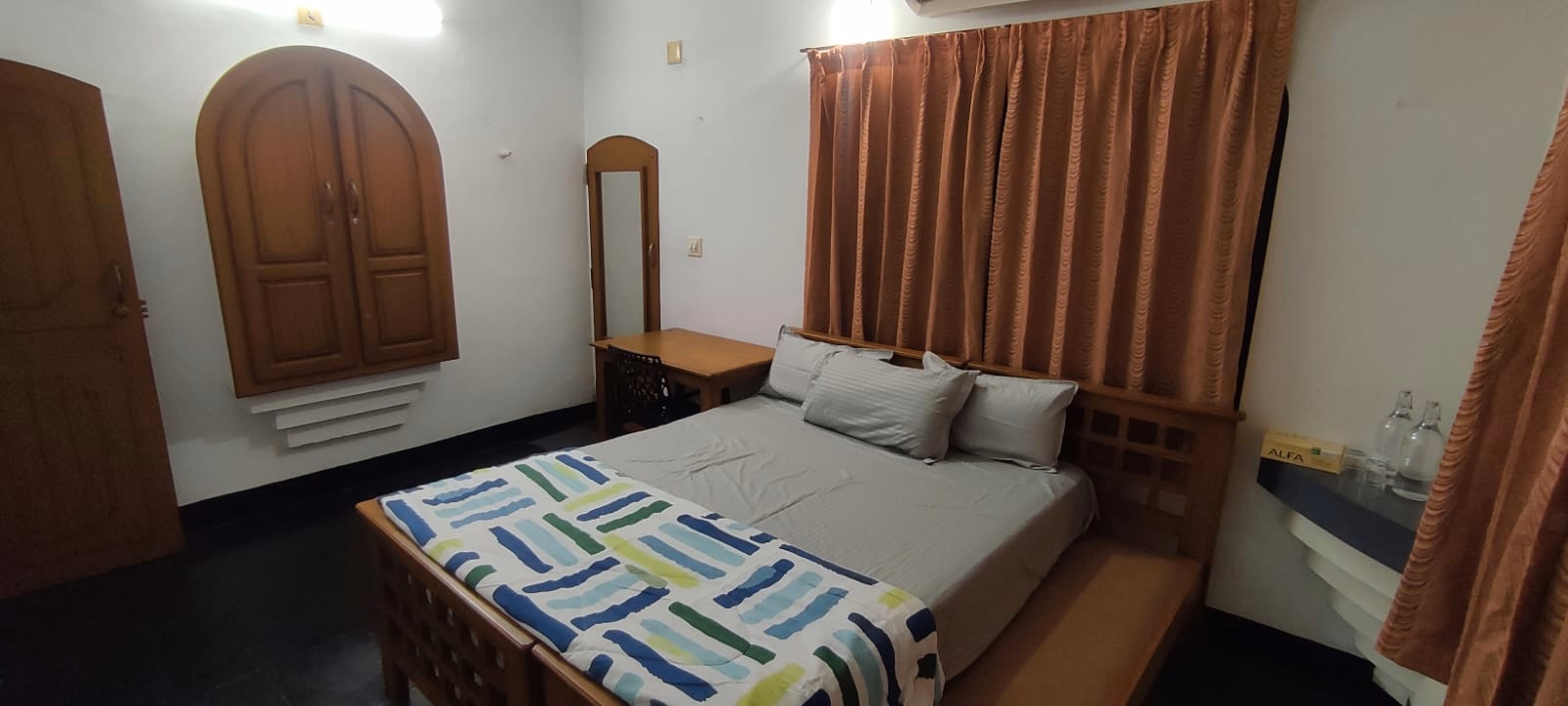 Bedroom with wooden bed, mirror, and warm curtains